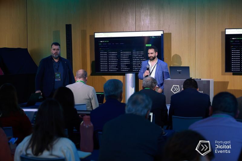 Demonstração do VIRIATUS em palco, com um painel de dados projetado e a assistência atenta