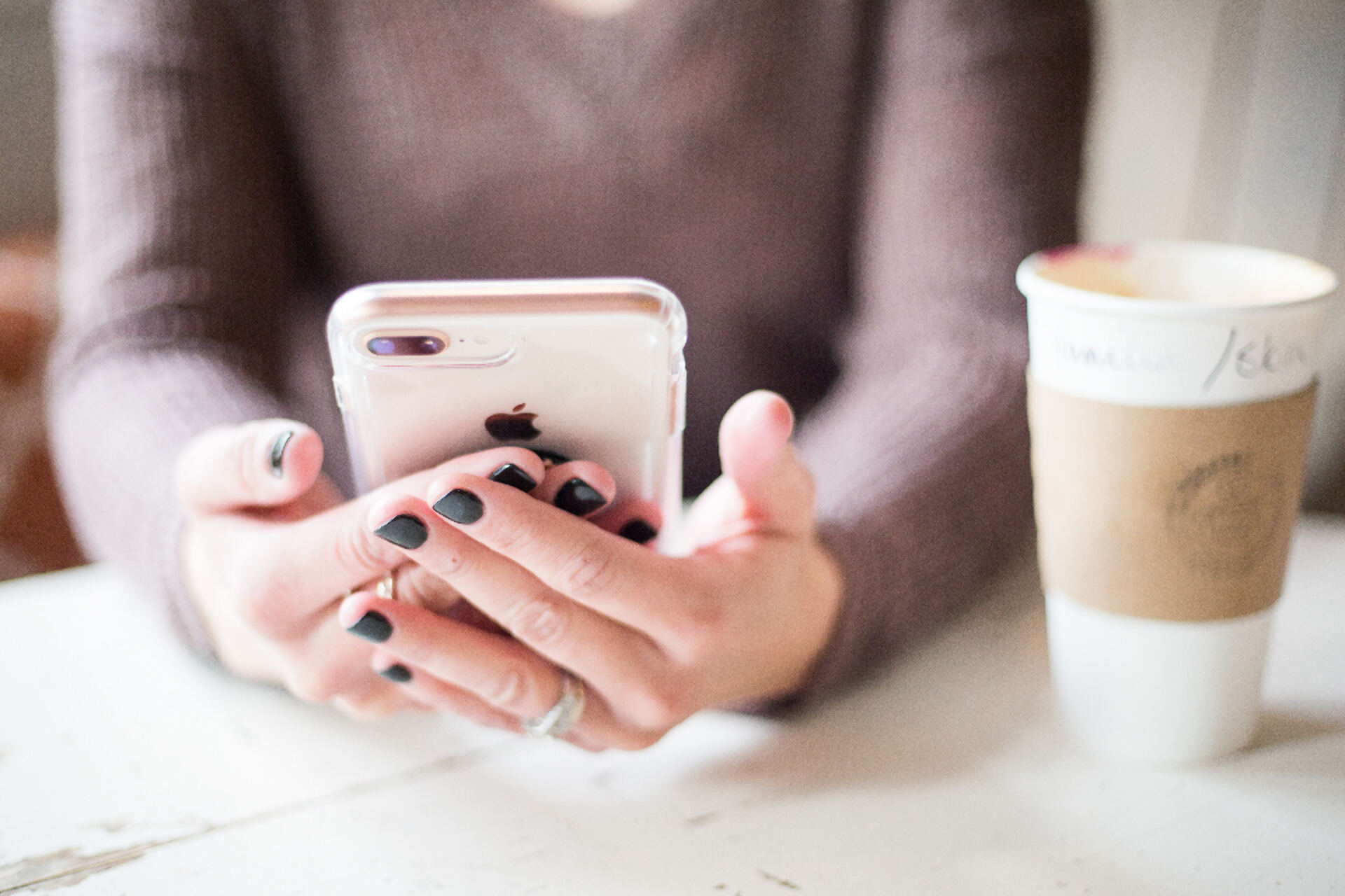 Mãos a usar um smartphone junto a um café